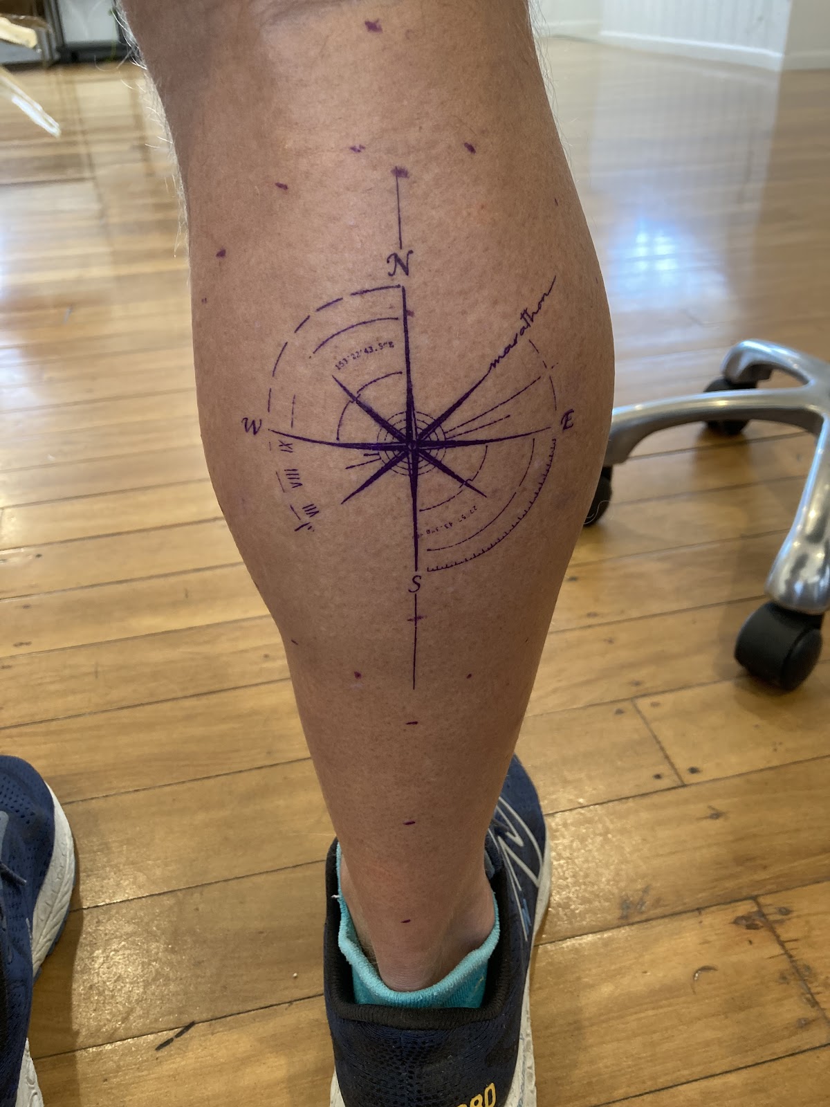 Compass rose tattooed in purple ink on a calf
